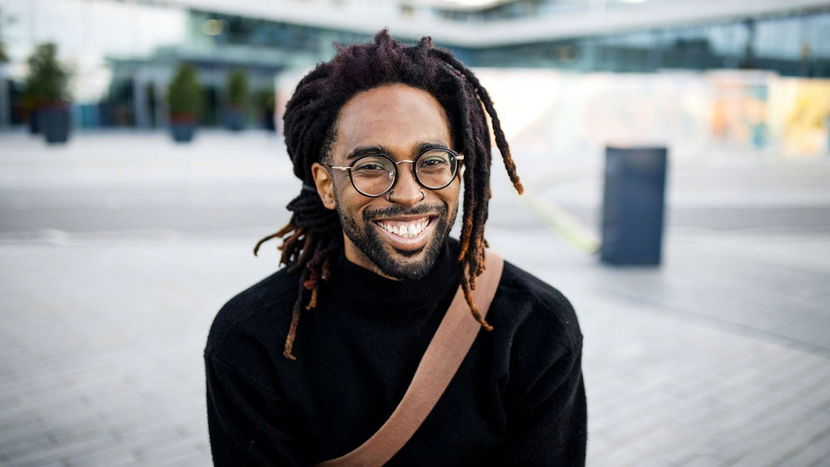 A Black man with thick, textured dreadlocks featuring natural dark purple-brown tones and sun-kissed, lighter tips. 