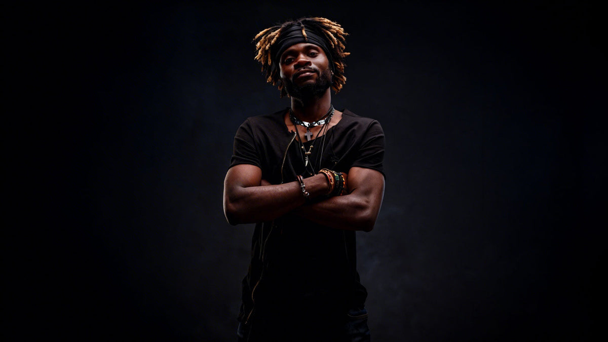 a Black man with golden-tipped dreadlocks, styled beneath a black headwrap, exuding a calm, confident demeanor